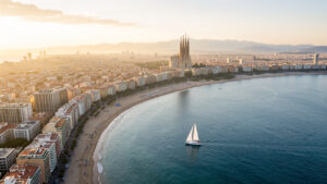 Vue aérienne réaliste de Barcelone au lever du soleil, avec une plage urbaine, un voilier sur la Méditerranée et la silhouette de la Sagrada Família au loin.